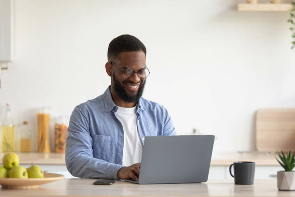 Satisfeito jovem afro-americano barbudo homem com óculos trabalhando no laptop - Foto, Imagem