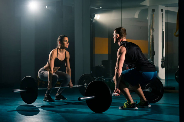 Una mujer y un hombre entrenando juntos y simultáneamente haciendo ejercicio de levantamiento de pesas en el gimnasio. - Foto, Imagen