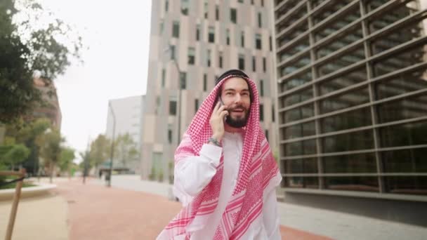 Usmívající se arabský muž těší telefonát konverzace venku, chůze City Street v Dubaji - Záběry, video