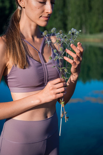 Giovane ragazza bruna tenera con un ramo a base di erbe davanti al suo viso in piedi vicino al lago. - Foto, immagini