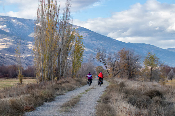Osoyoos, BC, Canada - November 10, 2021: Two people on e-bikes enjoying a cold November ride on the International Hike and Bike Trail in the Okanagan Valley - Fotoğraf, Görsel