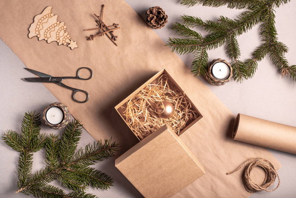 Pakowanie prezentu na Boże Narodzenie i Nowy Rok w materiały przyjazne dla środowiska: papier kraft, żywe gałązki jodły, stożek, szpagat. Tagi z makiety, naturalny wystrój, ręcznie, flatlay. - Zdjęcie, obraz