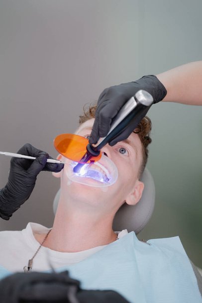 The dentist illuminates the patient's teeth with an ultraviolet lamp to fix the braces. - Foto, Bild