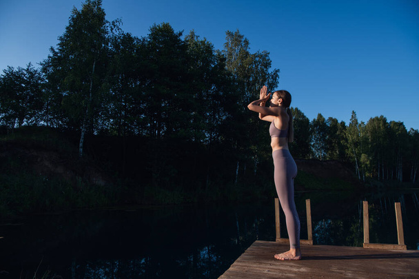 Krásná mladá žena předvádí duchovní jógu pózovat na lesním jezeře za slunečného dne, východ slunce zen wellness - Fotografie, Obrázek