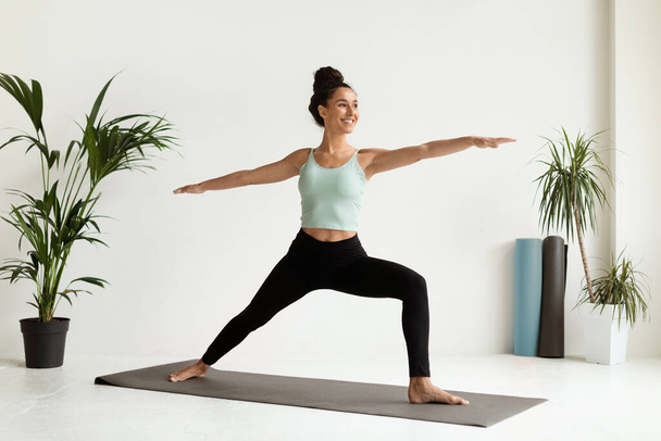 Belle jeune femme pratiquant le yoga, debout dans la posture guerrière sur tapis de fitness - Photo, image