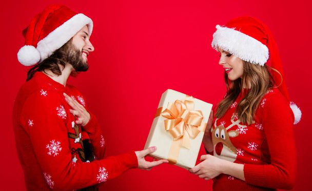 Αϊ-Βασίλη ζευγάρι σε χριστουγεννιάτικο καπέλο με δώρο κουτί. Φίλοι άντρας γυναίκα σε κόκκινο πουλόβερ με το δώρο της Πρωτοχρονιάς. - Φωτογραφία, εικόνα