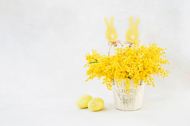 Easter decoration and mimosa flowers bouquet on a light background. Greeting card, copy space - Foto, Imagem