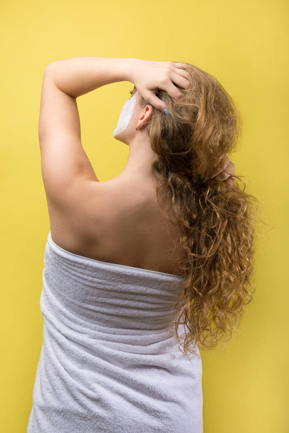 Meisje met een cosmetisch masker op haar gezicht in een witte handdoek. - Foto, afbeelding