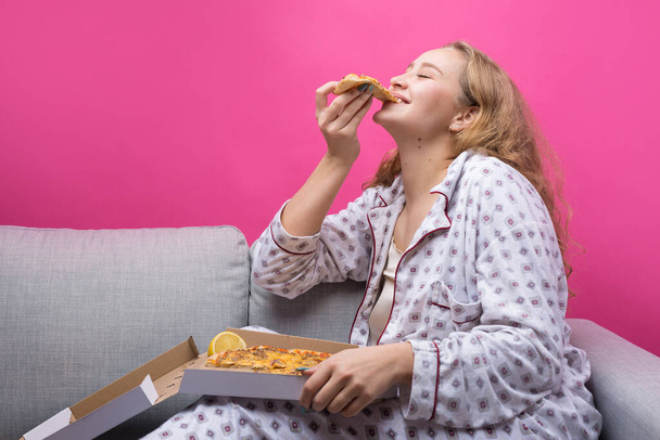 Tyttö istuu sohvalla ja syö pizzaa.. - Valokuva, kuva