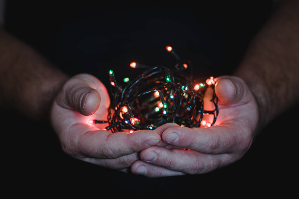 férfi kezek kezében egy karácsonyi koszorú fények egy sötét háttér másolási hely szöveges. Retro effektus, közelkép. Tél, képeslap sablon - Fotó, kép