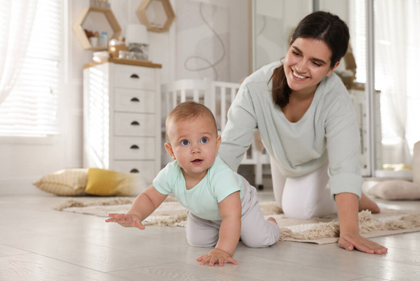 Happy young mother watching her cute baby crawl on floor at home - Foto, afbeelding