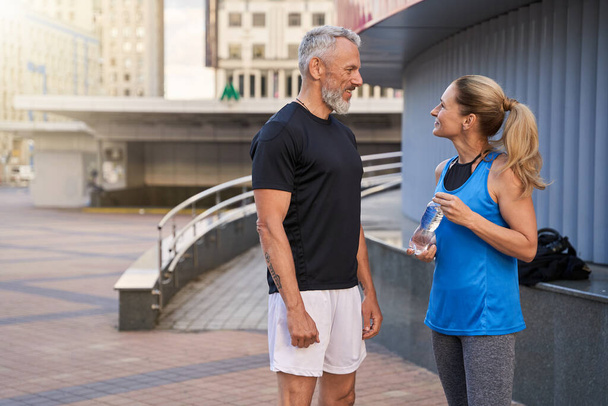 スポーツウェアの男と女が互いに笑顔で、一緒に屋外で準備ができて立ってトレーニングのために - 写真・画像