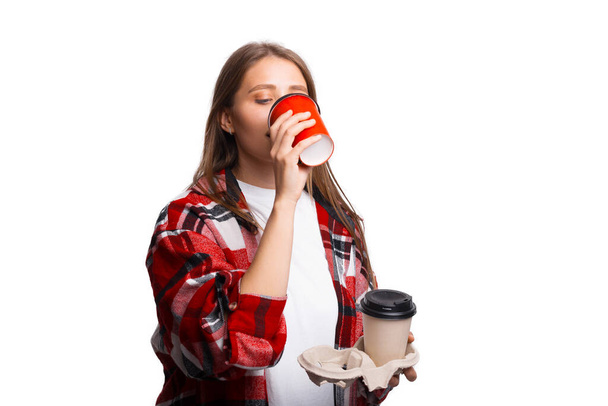 Mujer joven bebiendo taza de café, sosteniendo llevar titular con taza, fondo blanco - Foto, Imagen
