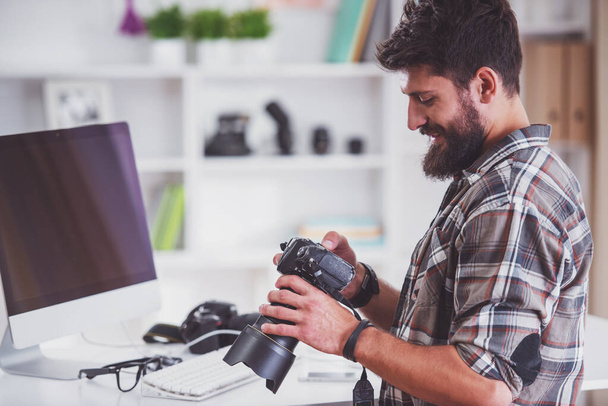 Молодой веселый фотограф с бородой, работая в офисе
 - Фото, изображение