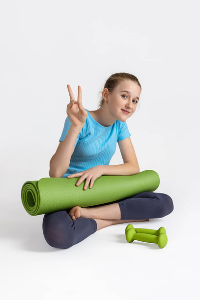 Positive teen girl is ready for yoga classes. Green dumbbells and exercise mat. - Fotoğraf, Görsel