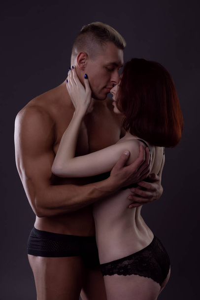 Sexy young couple in love in underwear in a fit of tender passion on a dark background - Photo, image