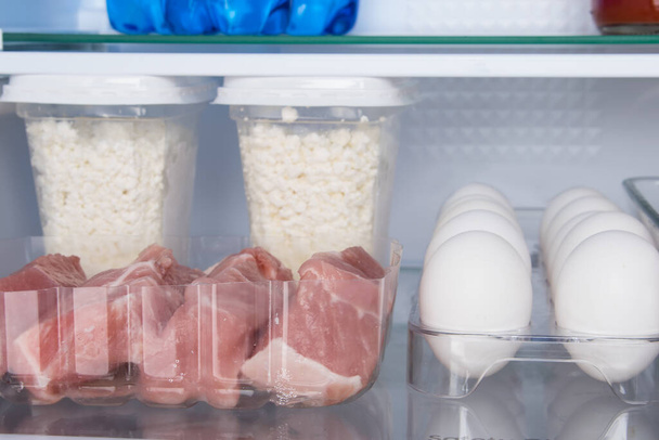 close-up, on the background of a white refrigerator, lie products, meat, eggs and cottage cheese - Фото, зображення