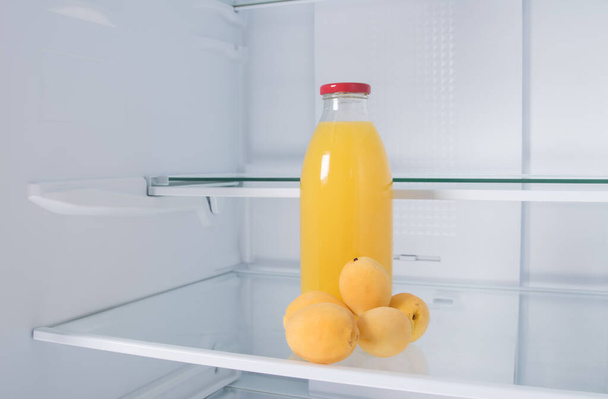 against the background of a white refrigerator, there is a bottle of juice and apricots on a glass shelf, close-up - Foto, afbeelding