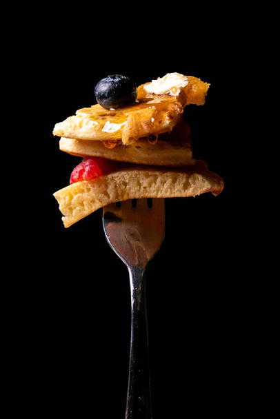 A vertical shot of pancake with berries and maple syrup on a black background - Fotó, kép