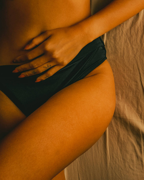 A vertical closeup shot of a tan female laying in bed in underwear - Fotó, kép