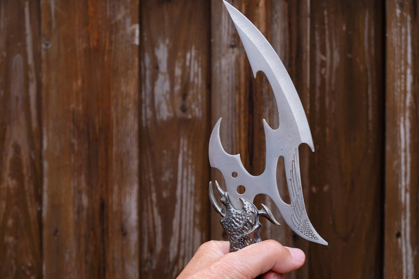 Dekorativní nůž zajímavého designu v mužské ruce na dřevěném pozadí. Vítězné gesto. Kopírovat prostor. - Fotografie, Obrázek