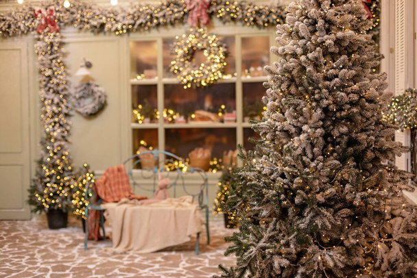 Das schneebedeckte Haus ist für das neue Jahr dekoriert. Vintage-Winterhof, dekoriert mit Neujahrsschmuck, Weihnachtsbäumen, Laternen und einer gemütlichen Bank. Weiche selektive Fokussierung. - Foto, Bild