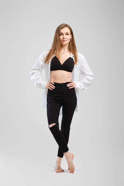 Full length studio portrait of young barefoot woman in black jean and shirt - Фото, зображення