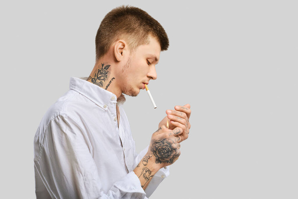 Young tattooed man lights a cigarette in the studio - Фото, зображення