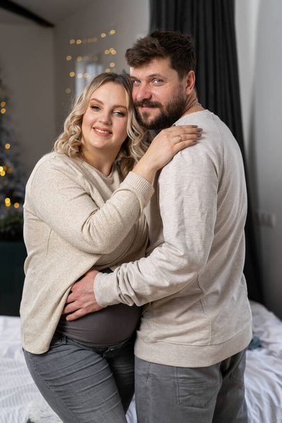 Happy family concept. Husband hug belly pregnant wife standing indoor living room near sofa Caucasian man and woman pregnancy and new life concept. Love and care  - Foto, imagen