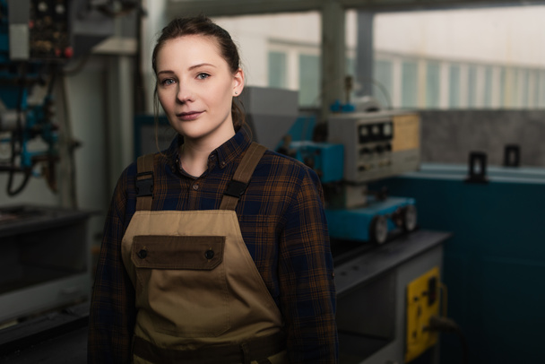 Young welder in uniform looking at camera in blurred factory  - Фото, изображение