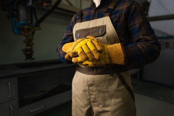 Обрезанный вид сварщика в перчатках и комбинезоне на заводе  - Фото, изображение