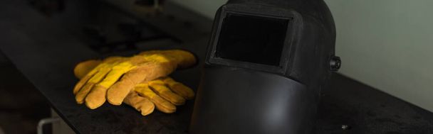 Guantes de soldadura y casco en la mesa en fábrica, banner  - Foto, Imagen