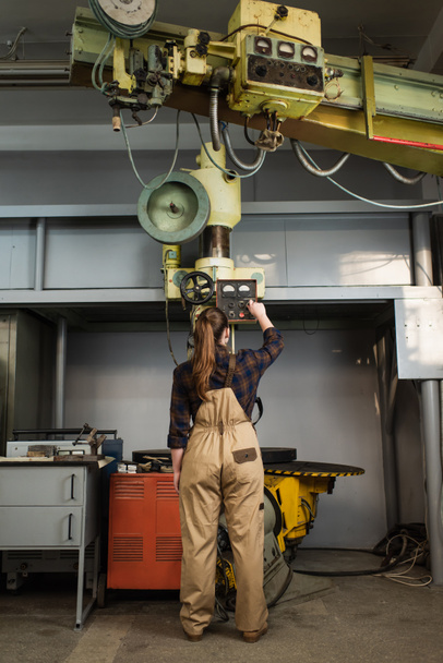 Vista posterior del soldador en overoles y camisa que trabaja en la máquina de soldadura en fábrica  - Foto, Imagen