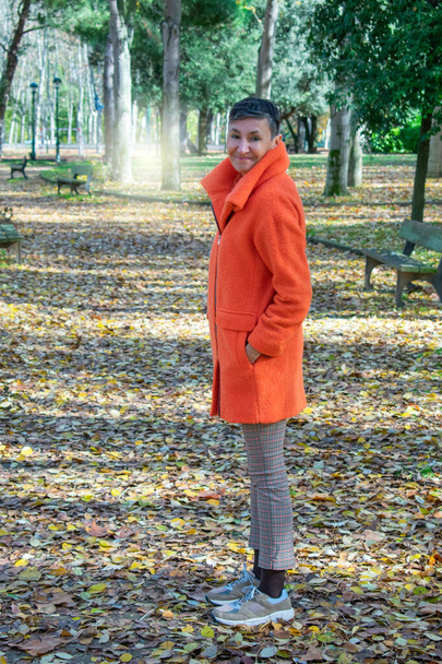 усміхнена зріла жінка з помаранчевим пальто в парку
 - Фото, зображення