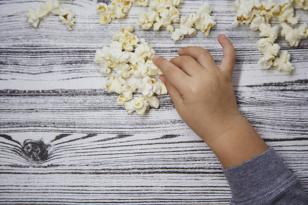 Kinderneugier. Kleinkind Hand versucht ein Popcorn. Nationaler Popcorn-Tag. Kopierraum. Ansicht von oben.  - Foto, Bild