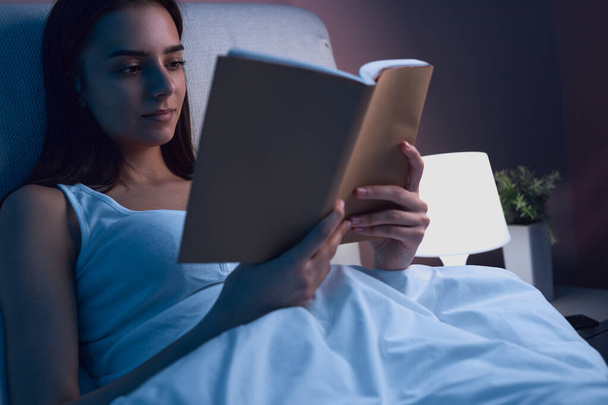 Woman reading book in bed before sleep - Fotó, kép
