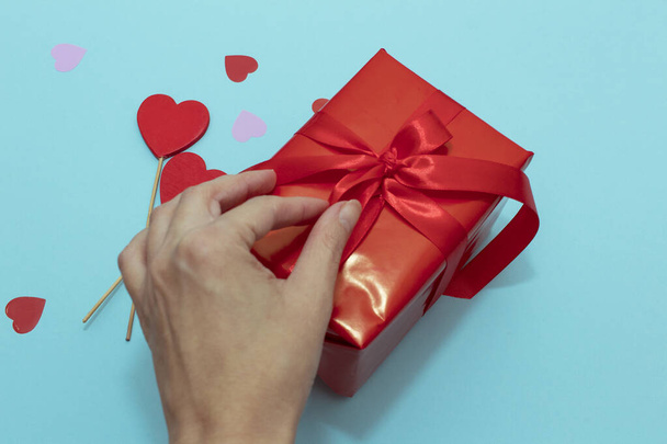 Red box with red ribbon on a blue paper background. Valentine's Day gift with confetti and decor - 写真・画像