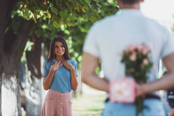 Молодую пару встречают на свидании с цветами и подарком в парке - Фото, изображение