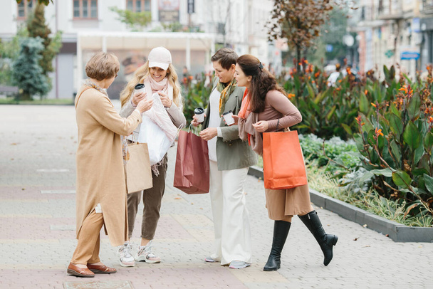 Egy csapat mosolygó felnőtt nő, akik bevásárlószatyrokat tartanak, miközben sétálnak a városban. - Fotó, kép