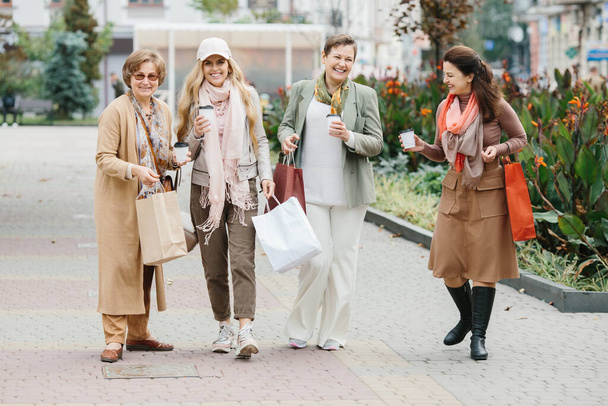 Un groupe de femmes adultes souriantes tenant des sacs à provisions tout en marchant dans la ville - Photo, image