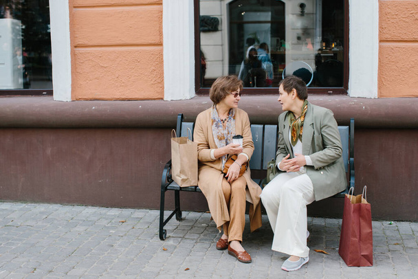 シニア女性親友楽しい議論ショッピングベンチに座って路上で - 写真・画像