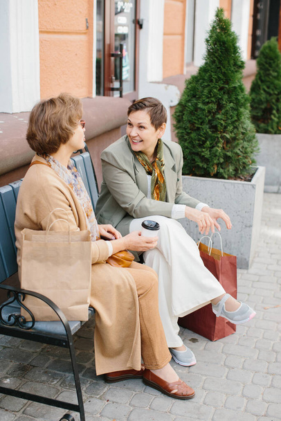 Senior femmes meilleurs amis avoir du plaisir à discuter shopping assis sur un banc dans la rue - Photo, image