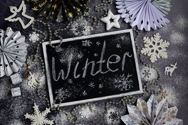 New Year and Christmas concept. White snowflakes, New Year decor and handwritten Winter lettering. Chalk inscription on a black board. Top view - Foto, Bild