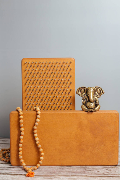 Bronze statue of Ganesha. Tibetan rosary, mala or japamala. Brown Sadhu wooden boards with nails for yoga and spiritual practices on the grey background. Meditation, standing on nails, therapy. - Photo, Image