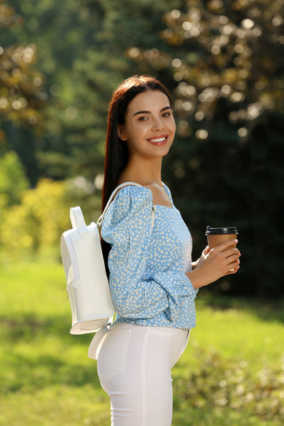 Süslü beyaz sırt çantası ve parkta kahvesiyle güzel bir genç kadın. - Fotoğraf, Görsel