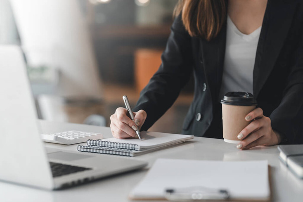 Primer plano de la mano de una mujer de negocios sosteniendo una taza de café mientras toma notas en la oficina. - Foto, imagen