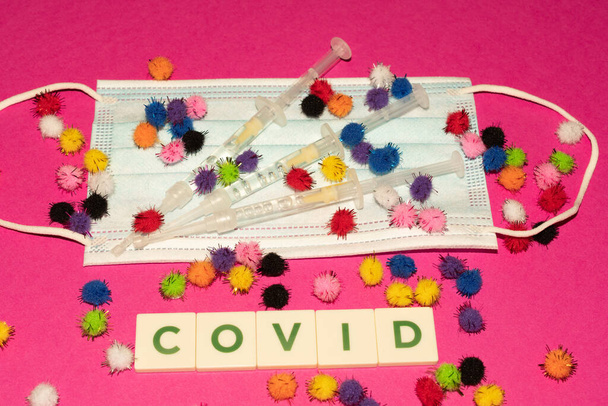 Vaduz, Liechtenstein, December 17, 2021 Virus mutations on a medical face mask and syringes with the written word Covid - Foto, Imagem