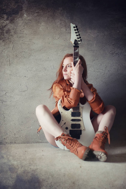 Молодая рыжая девушка с электрогитарой. Рок-музыкантка в кожаной куртке. Она красивая певица и исполнительница рок-музыки.
 - Фото, изображение