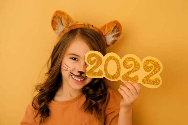 Egy vidám csinos lány festett bajusszal és tigris fülekkel becsukja az egyik szemét a 2022-es év számaival. A tigrisállat éve a kínai horoszkóp szerint. - Fotó, kép