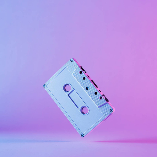 Colorful artistic still life of an old audio cassette balancing in edge over a graduated purple background - Photo, image